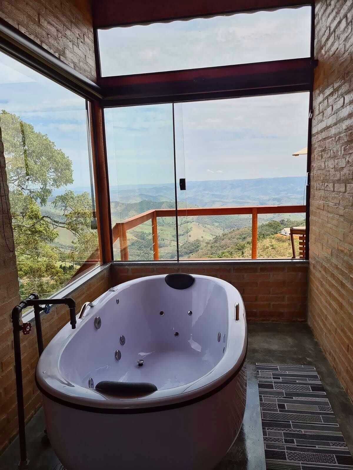 Banheira de hidromassagem branca em sacada de vidro de canto, com vista em camadas para as cristas da Serra da Mantiqueira